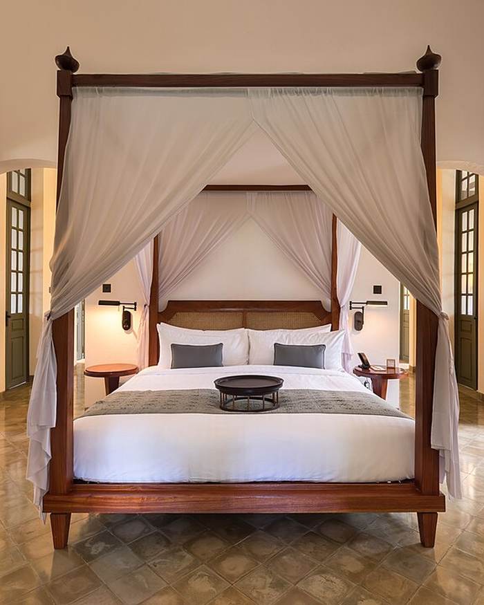 A four-poster bed with white drapes in a calm hotel room